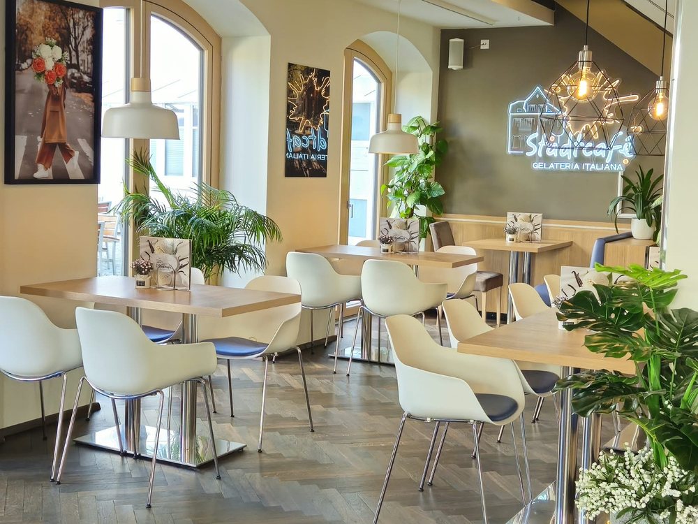 Gastraum des Stadtcafés mit Sitzgruppen, Pflanzen und Leuchtschriftzug
