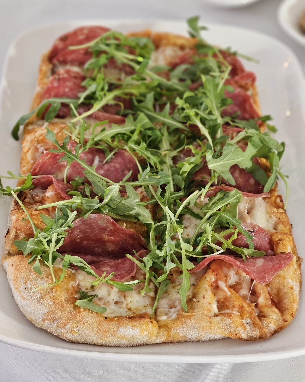 Pinsa Salami mit Rucola, Salami und Mozzarella auf dem Teller